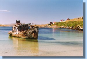 An old boat stranded on the beach. In the background the tiny settlement.