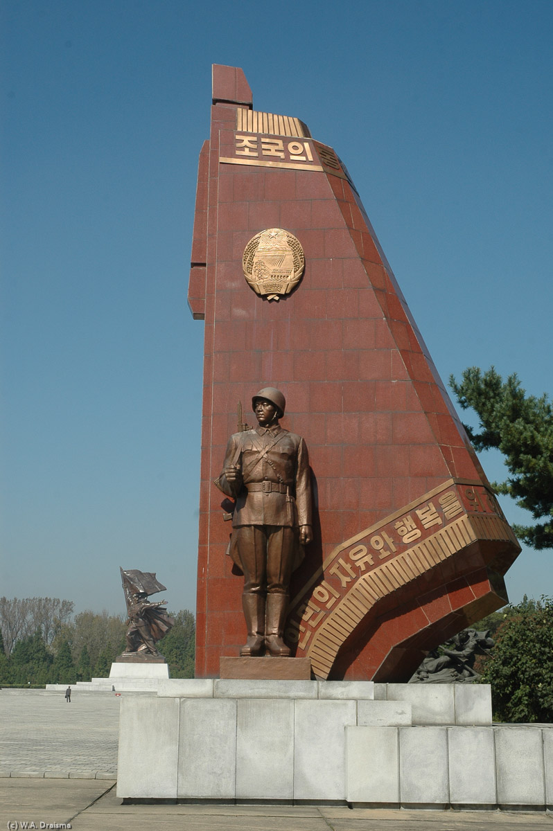 A soldier stands in front of the party flag with the "Victory" sculpture in the background.