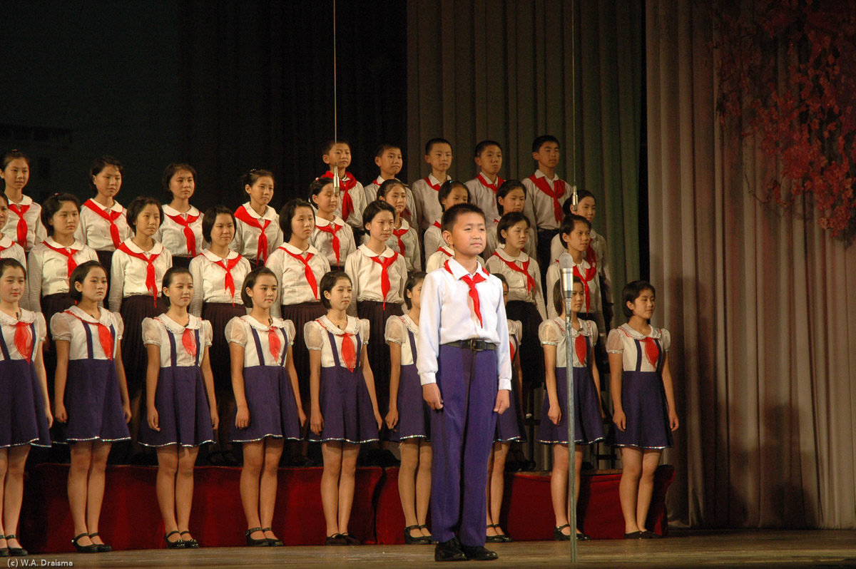 In front of a choir of singing students one soloist sings several songs. He has a clear and good voice. We cannot understand what he is singing but it's impressive nevertheless.