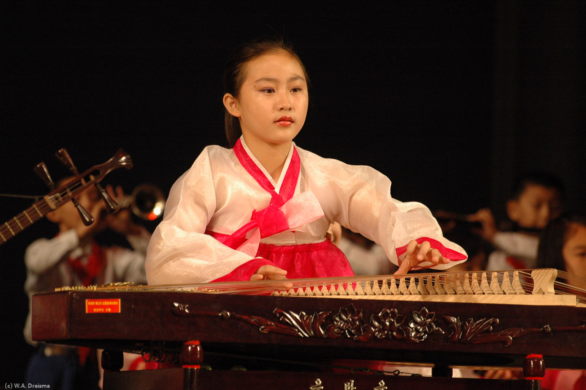 A girl playing another type of Gayageum. This one is put flat on a table instead of held on the player's knees.