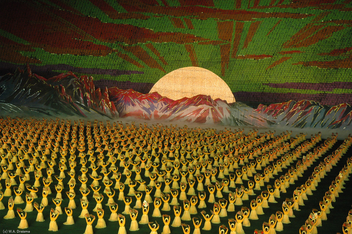 Formation of the rising sun. In the background the principle of the human pixel wall can be seen. The students carry a book with colored pages that is to be opened at a certain page at a certain moment.