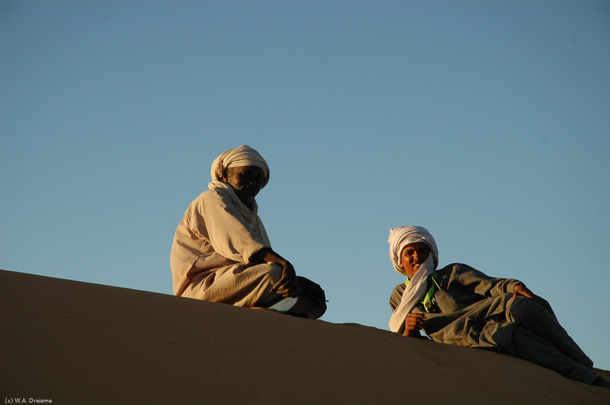 Our next destination will be the Ubari lakes in Idehan Ubari. On our way we pass Murzuq, another famous place in caravan history. A few kms past Murzuq we leave the road and set up camp between the sanddunes. Bilal (right), our travel agent, and Grandpa (left), the boss of the crew look at us.